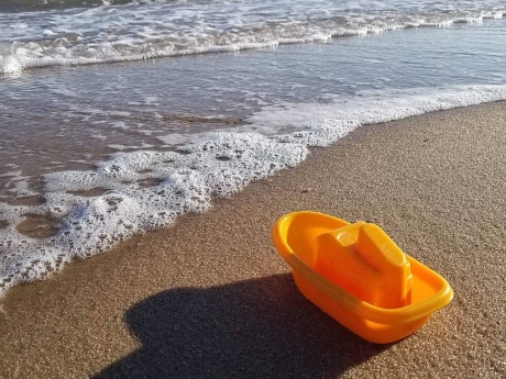 Orange toy on beach with waves approaching
